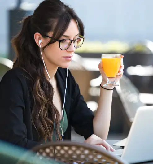 Knjigovodstvene usluge lijepa mlada žena pije sok od naranče dok radi sa svojim laptopom u kafiću